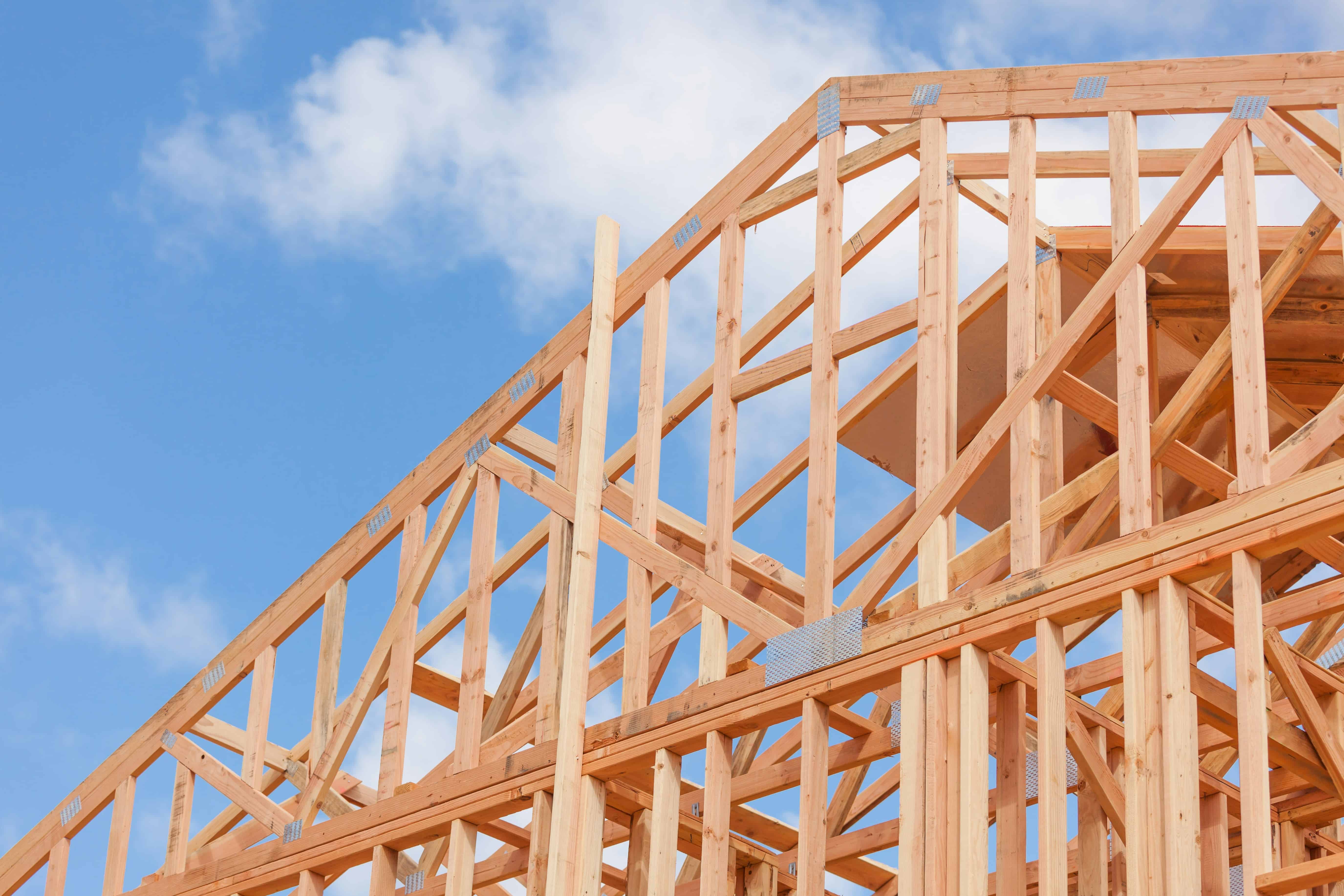 Wood framing for a house under construction with blue sky background.