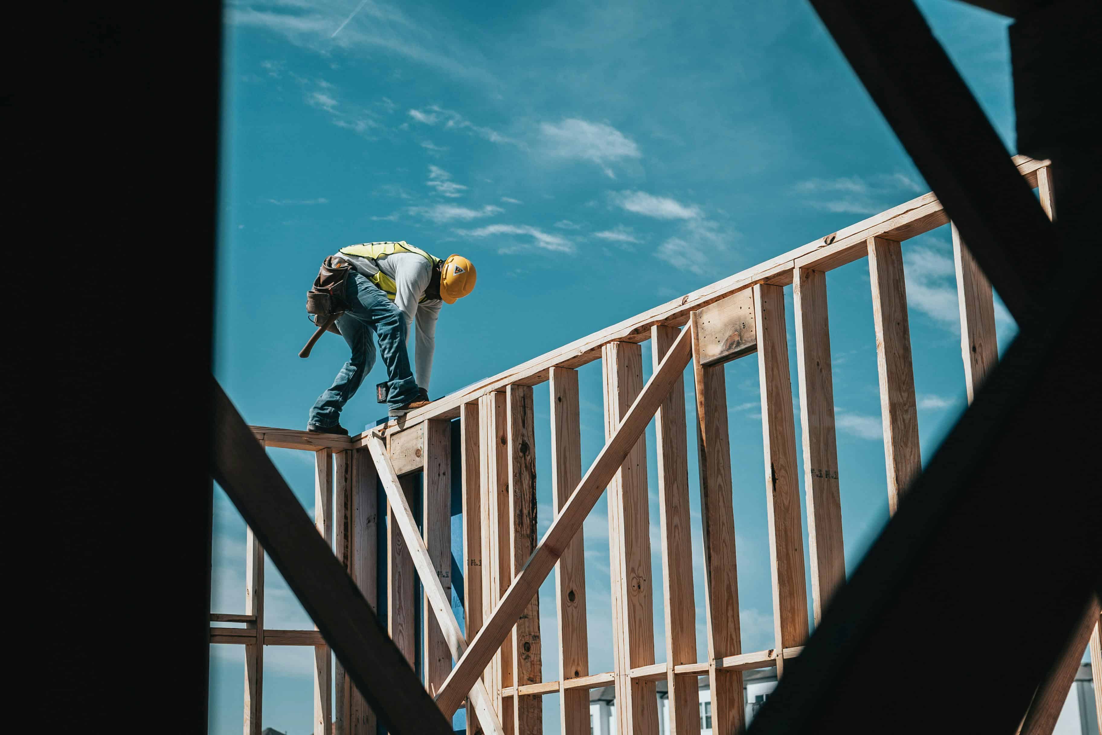 Worker in safety gear building a wooden frame for a commercial structure.