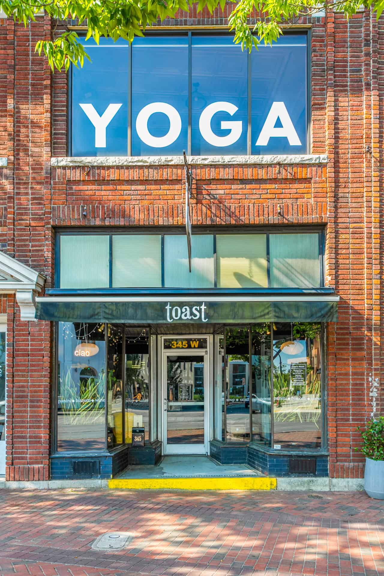 Yoga studio sign on brick building with large windows and green trees.