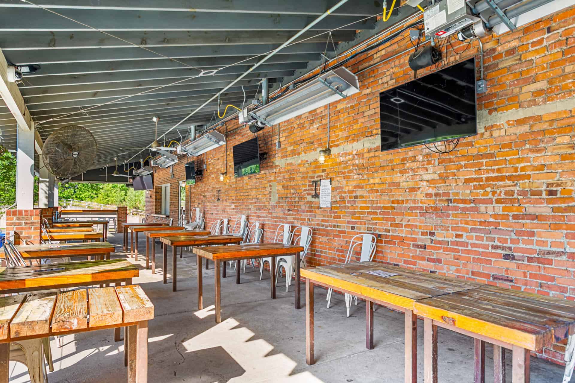 Outdoor dining space with wooden tables and metal chairs against a brick wall.