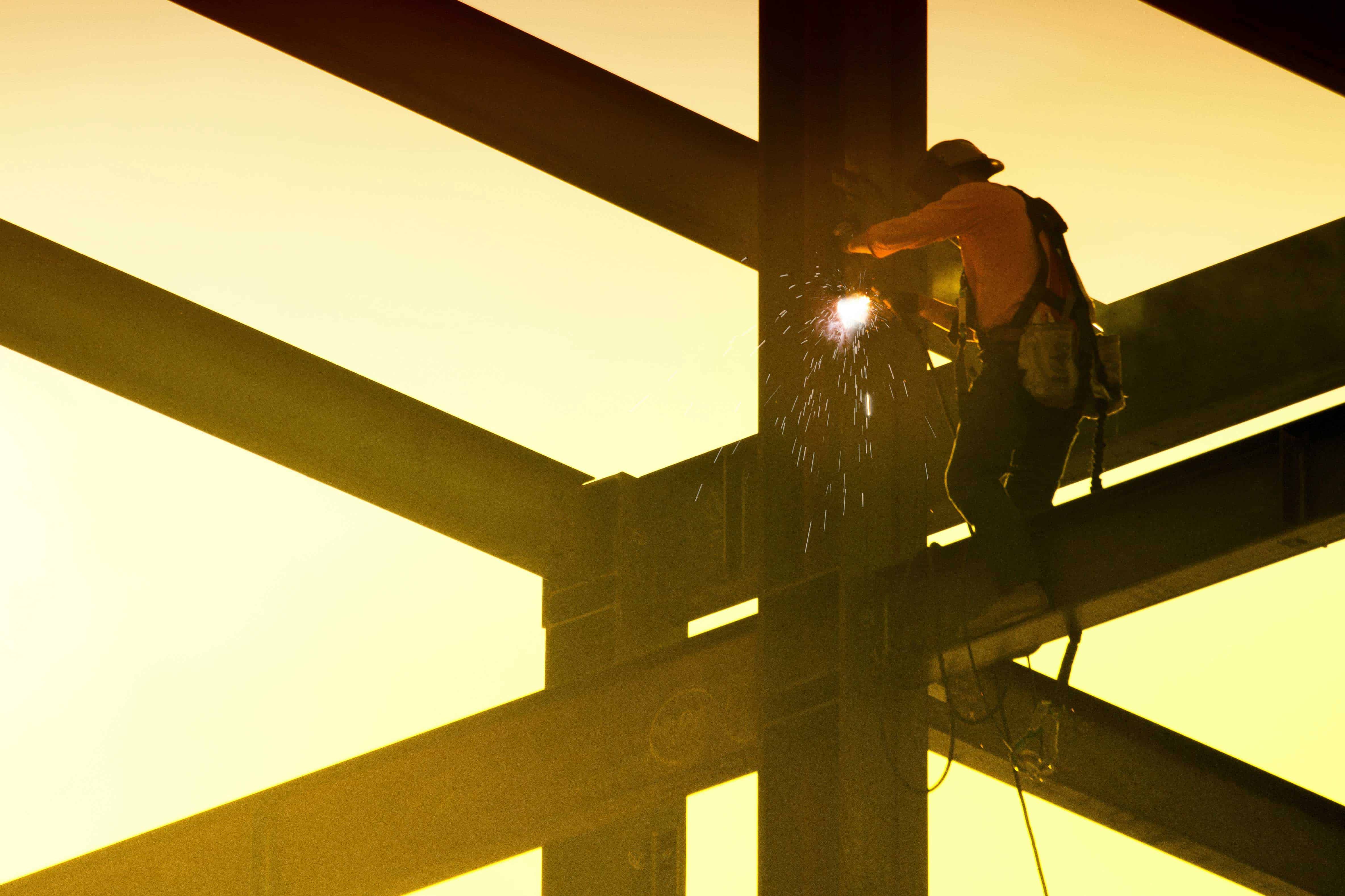 Construction worker welding steel beams at sunset for building framework.